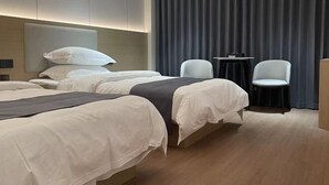 A hotel room with two beds, a small table, two chairs, and a dark curtain backdrop. - Meike Hotel (Wenzhou)