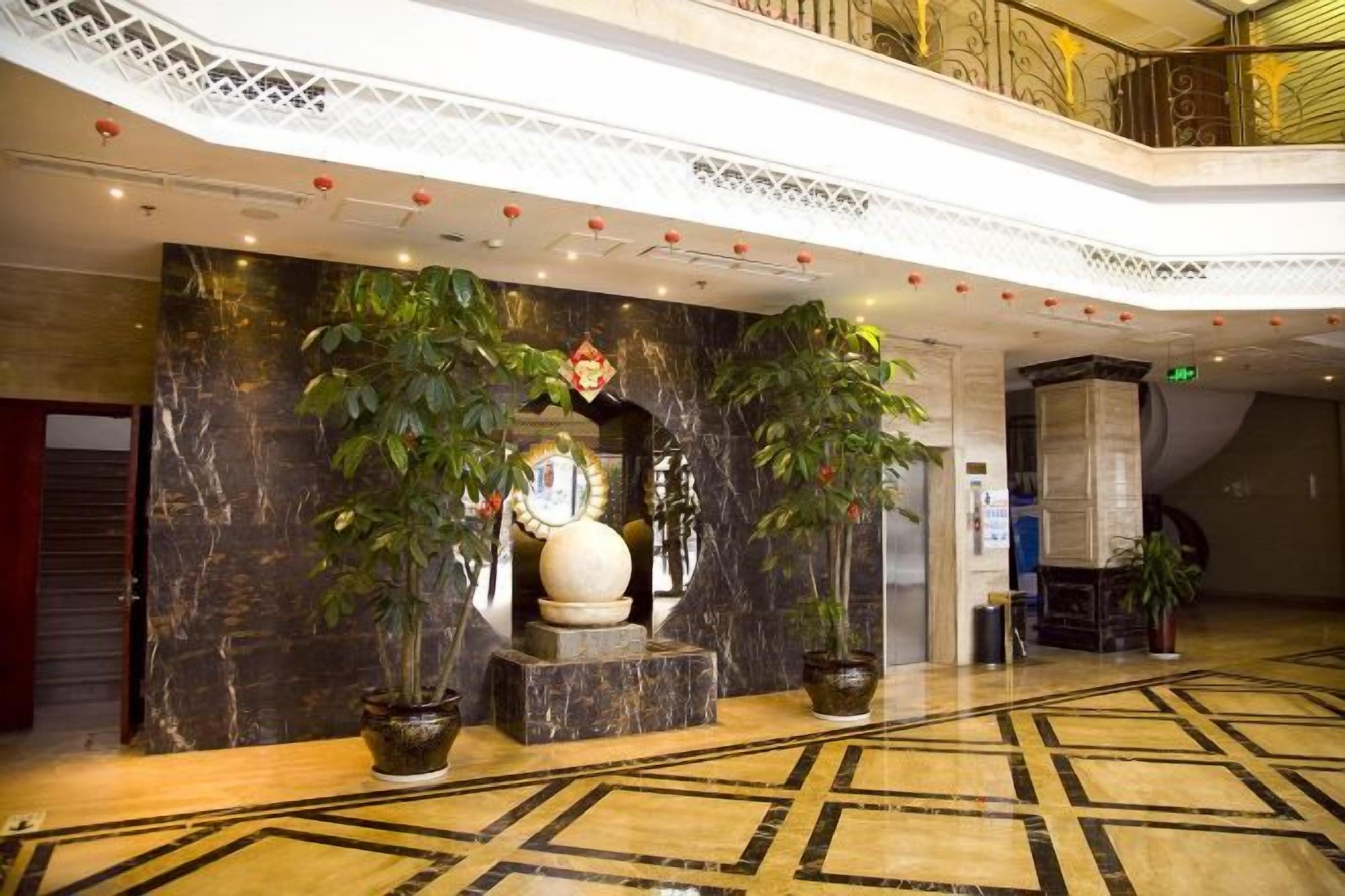 A lobby with marble flooring, a reception desk, and potted plants.
