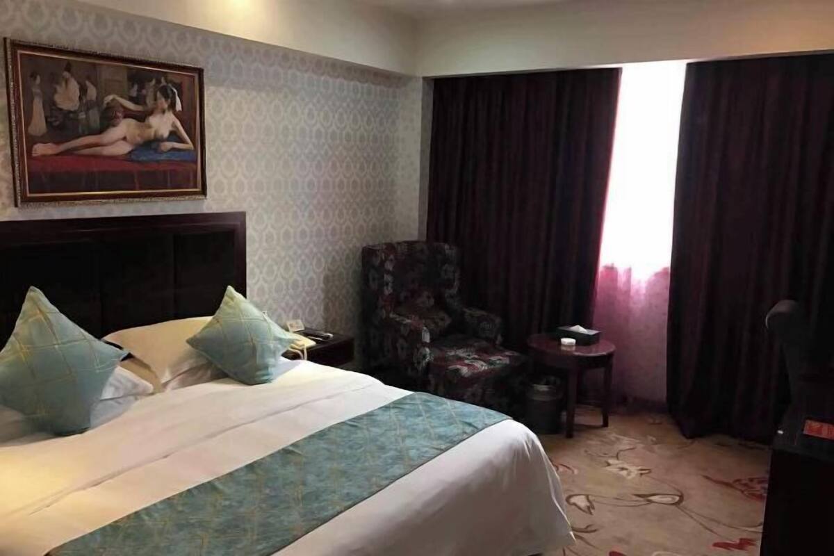 A hotel room with a bed, a chair, a small table, and a painting on the wall.