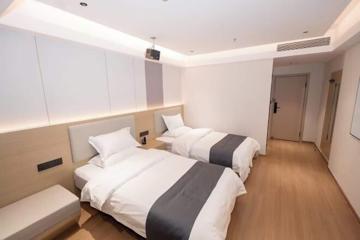 A hotel room with two beds, a bench, a ceiling projector, and a door.