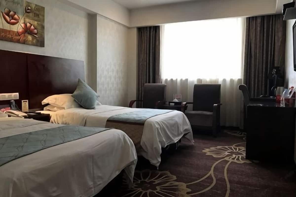 A hotel room with two beds, a desk, a chair, a dresser, and a large window with curtains.