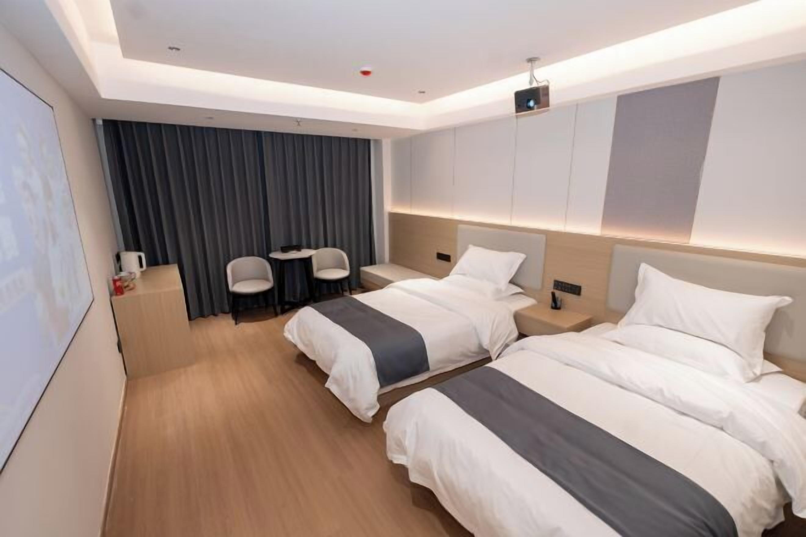 A hotel room with two beds, a desk, chairs, and a large window with curtains.