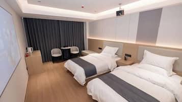 A hotel room with two beds, a desk, chairs, and a large window with curtains.