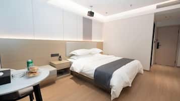 A modern hotel room with a bed, bedside table, and a small desk with a chair.