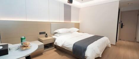 A modern hotel room with a bed, bedside table, and a small desk with a chair.