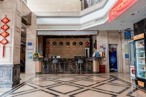 A hotel lobby with a reception desk, a vending machine, and a decorative wall.