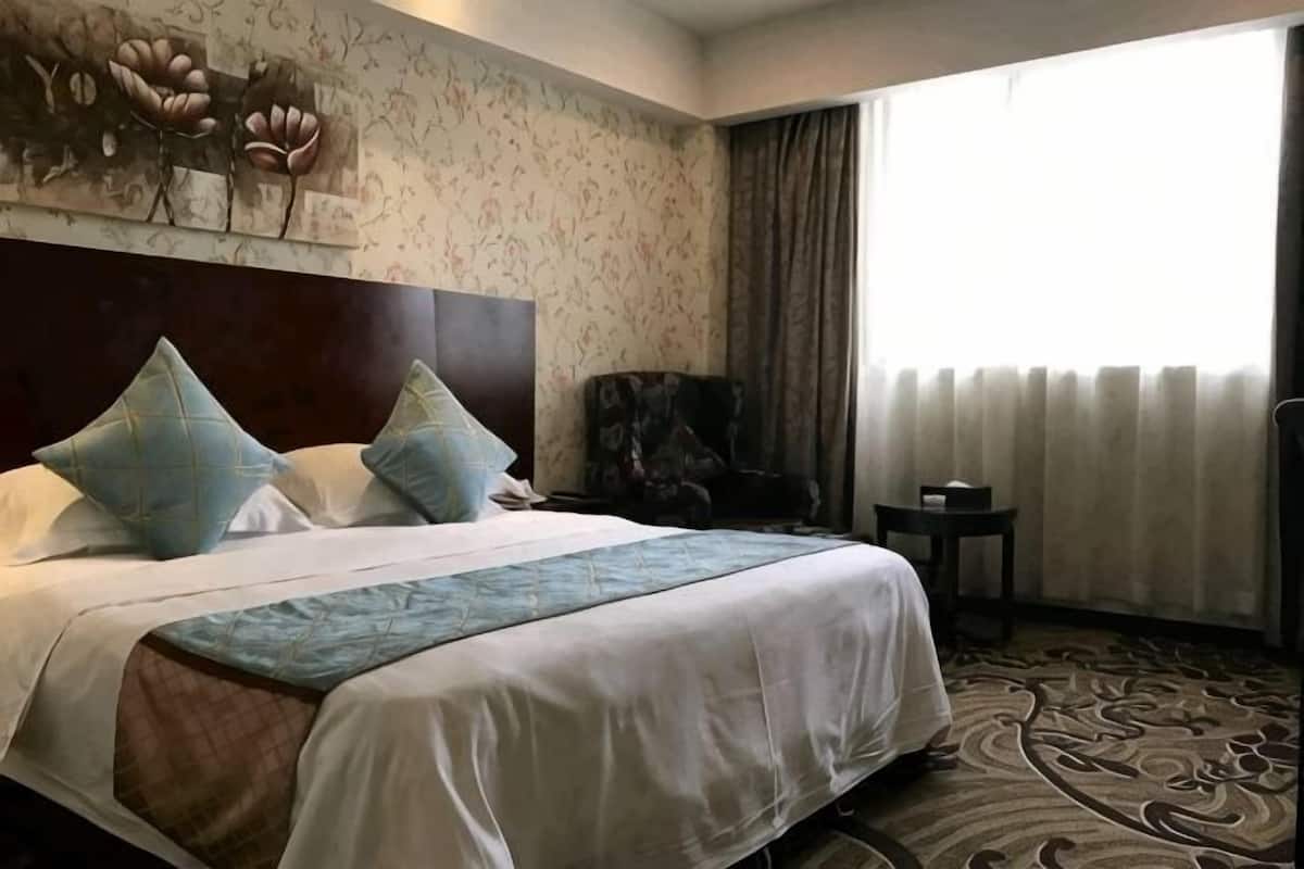 Habitación de hotel con una cama grande, cabecero, una silla, una mesita y una ventana con cortinas.