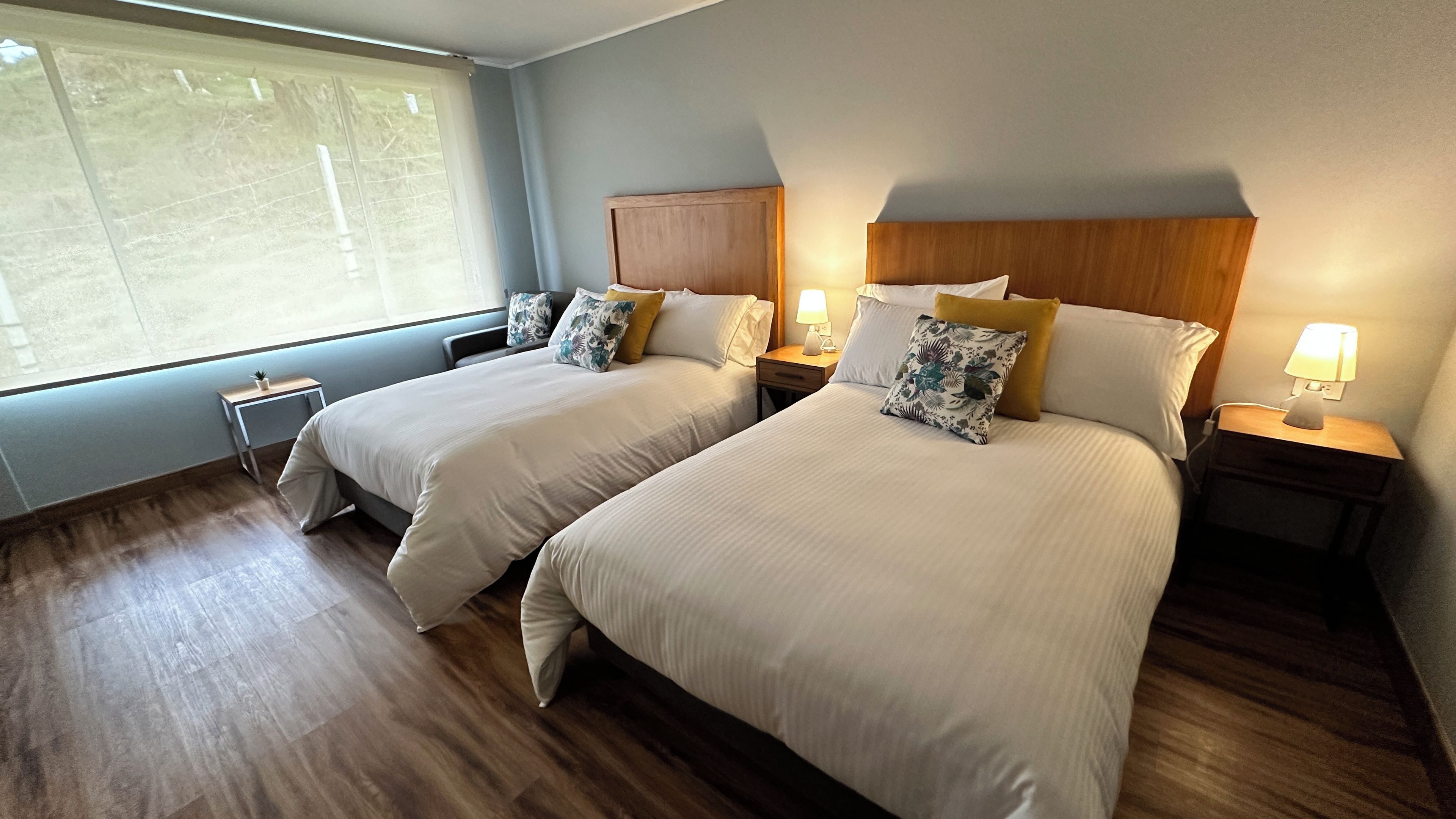Une chambre d’hôtel avec deux lits, deux tables de chevet, une petite table et une fenêtre.