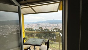 A balcony with a table and chairs, overlooking a cityscape with buildings and mountains in the distance. - Di Carbone Hotel Gastrobar (Facatativá)