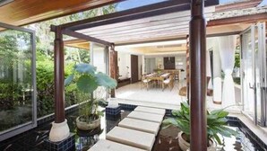 A modern outdoor patio area with a wooden pergola, potted plants, and a dining table. - Baan Leelawadee (Koh Samui)