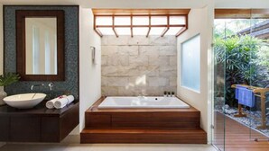 A modern bathroom with a freestanding bathtub, a large mirror, and a stone wall. - Baan Leelawadee (Koh Samui)