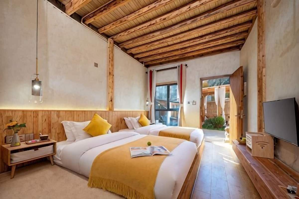 Una habitación con dos camas, techo de madera, televisión y ventana.