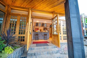 A wooden exterior with a stone staircase leading to a bar area with stools. - Lugu Huzi yueshanshe Inn (Ninglang)