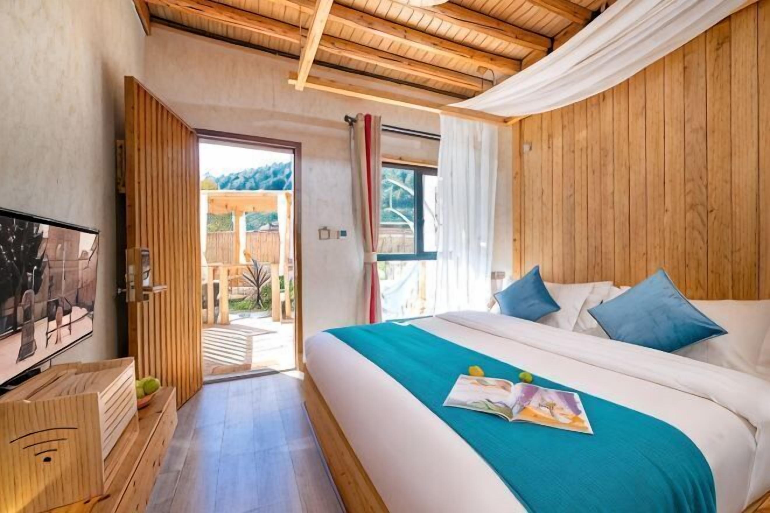 A bedroom with a bed, a television, a wooden dresser, and a view of the outdoors.