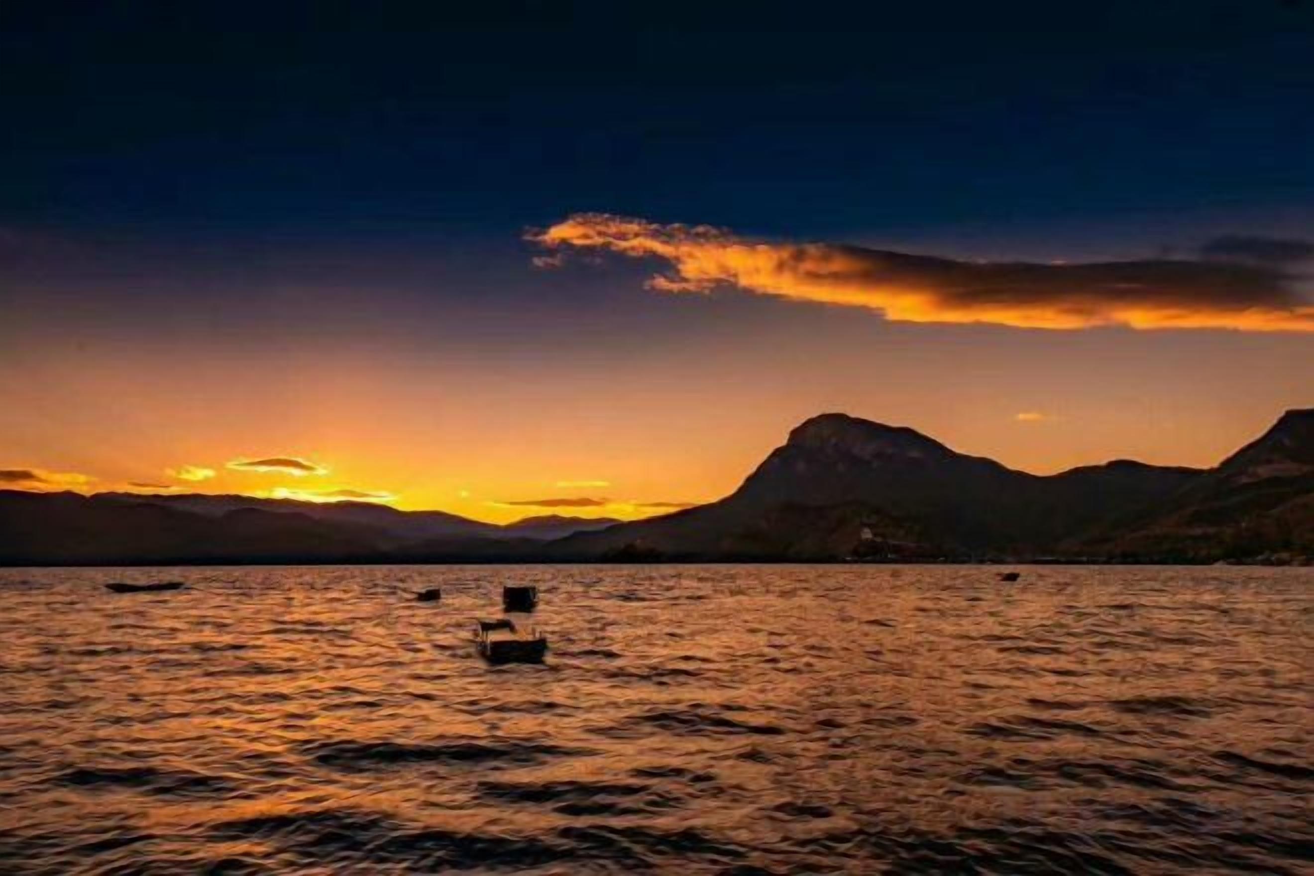Un atardecer sobre un cuerpo de agua con montañas al fondo.