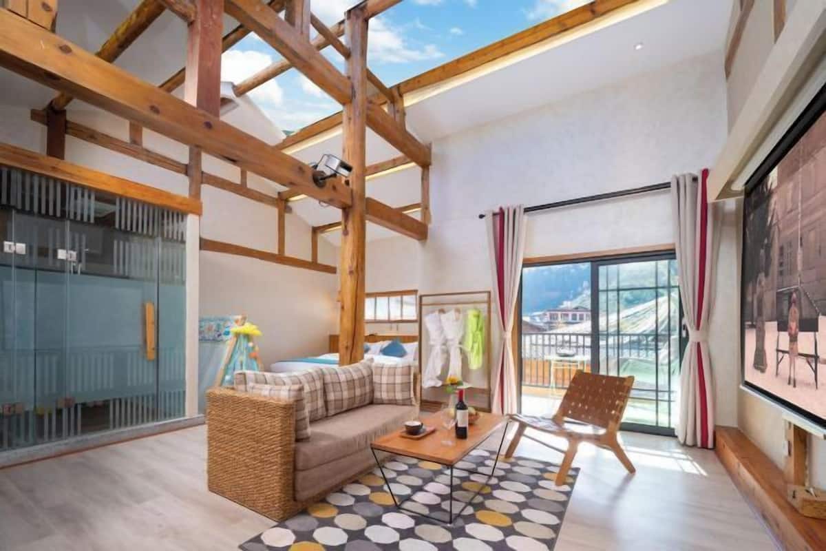 Una sala de estar moderna con vigas de madera a la vista, un sofá, una mesa de centro y un ventanal con cortinas.