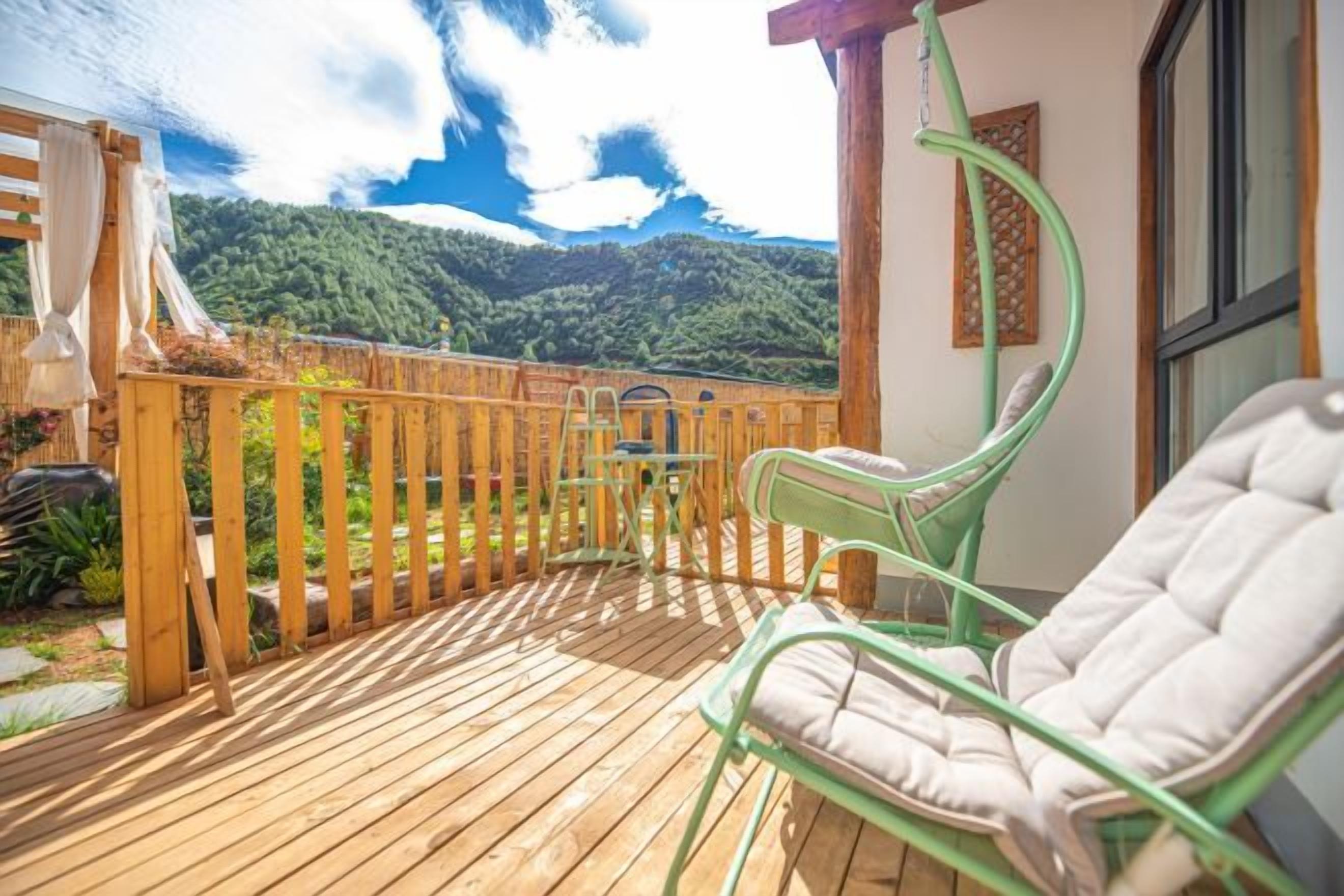 A wooden deck with a view of green hills, a hanging chair, and a table.