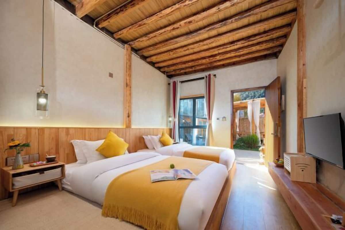 Habitación de hotel con dos camas, vigas de madera en el techo, un televisor y una pequeña mesa con lámpara.