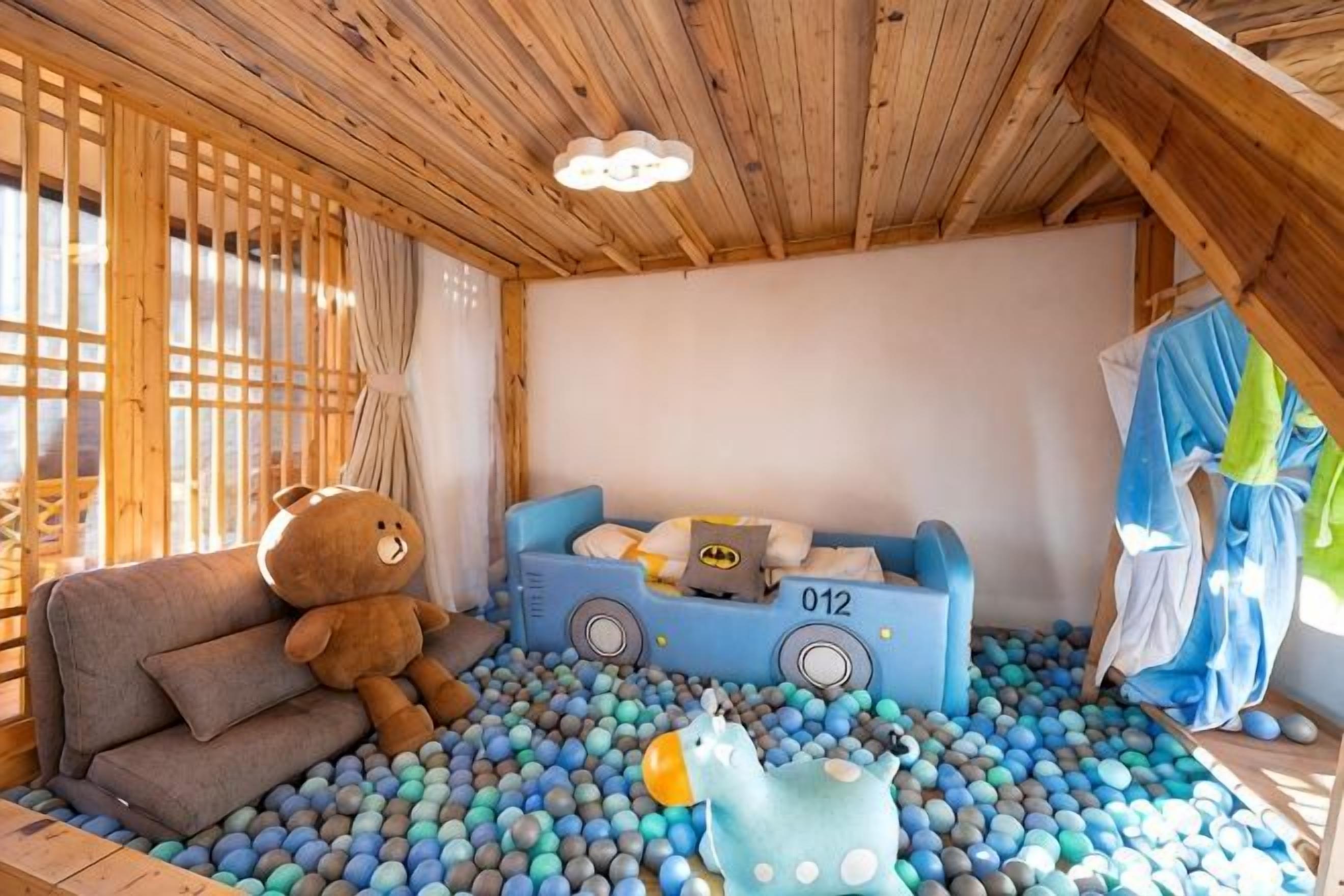 Una sala de juegos con una piscina de pelotas, un sofá, un gran osito de peluche y un coche de juguete.