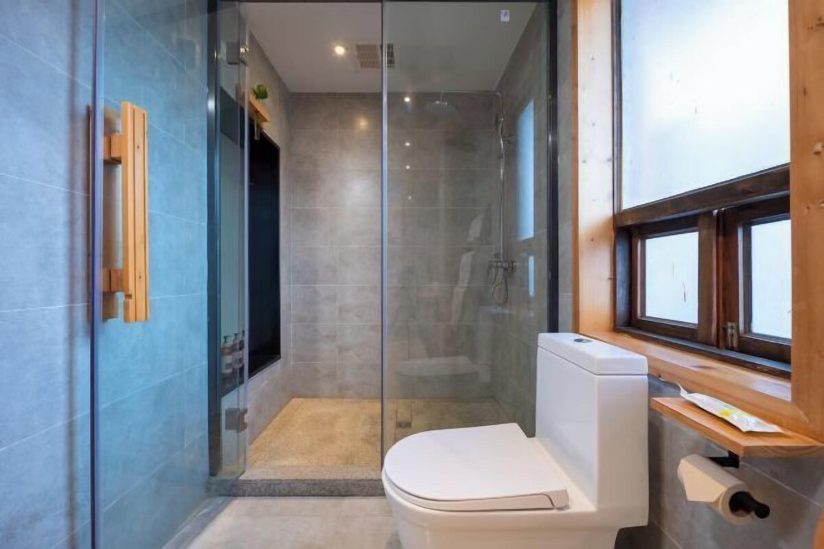 A modern bathroom with a glass shower enclosure, a toilet, and a window.
