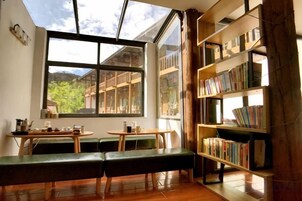 Una habitación con un ventanal grande, una estantería, un banco y una mesa.