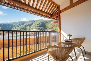 A balcony with a view of a forested valley, a wooden pergola, and wicker furniture. - Lugu Huzi yueshanshe Inn (Ninglang)