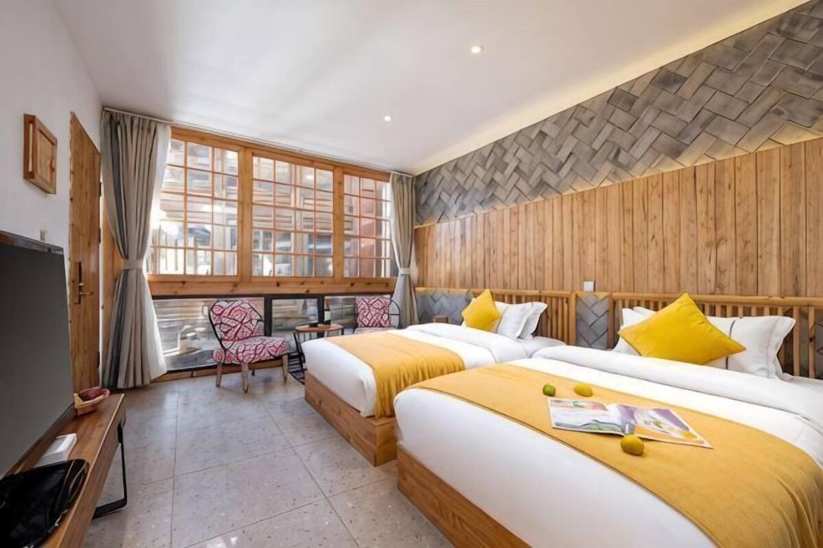 A hotel room with two beds, a TV, a desk, and a window with a city view.