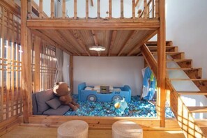 A cozy room with a wooden staircase, a sofa with a teddy bear, a blue toy car, and a ball pit. - Lugu Huzi yueshanshe Inn (Ninglang)