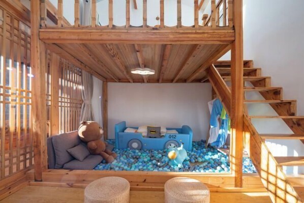 A cozy room with a wooden staircase, a sofa with a teddy bear, a blue toy car, and a ball pit. - Lugu Huzi yueshanshe Inn (Ninglang)