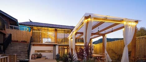 A modern house with a covered outdoor area, a staircase, and a fenced garden.