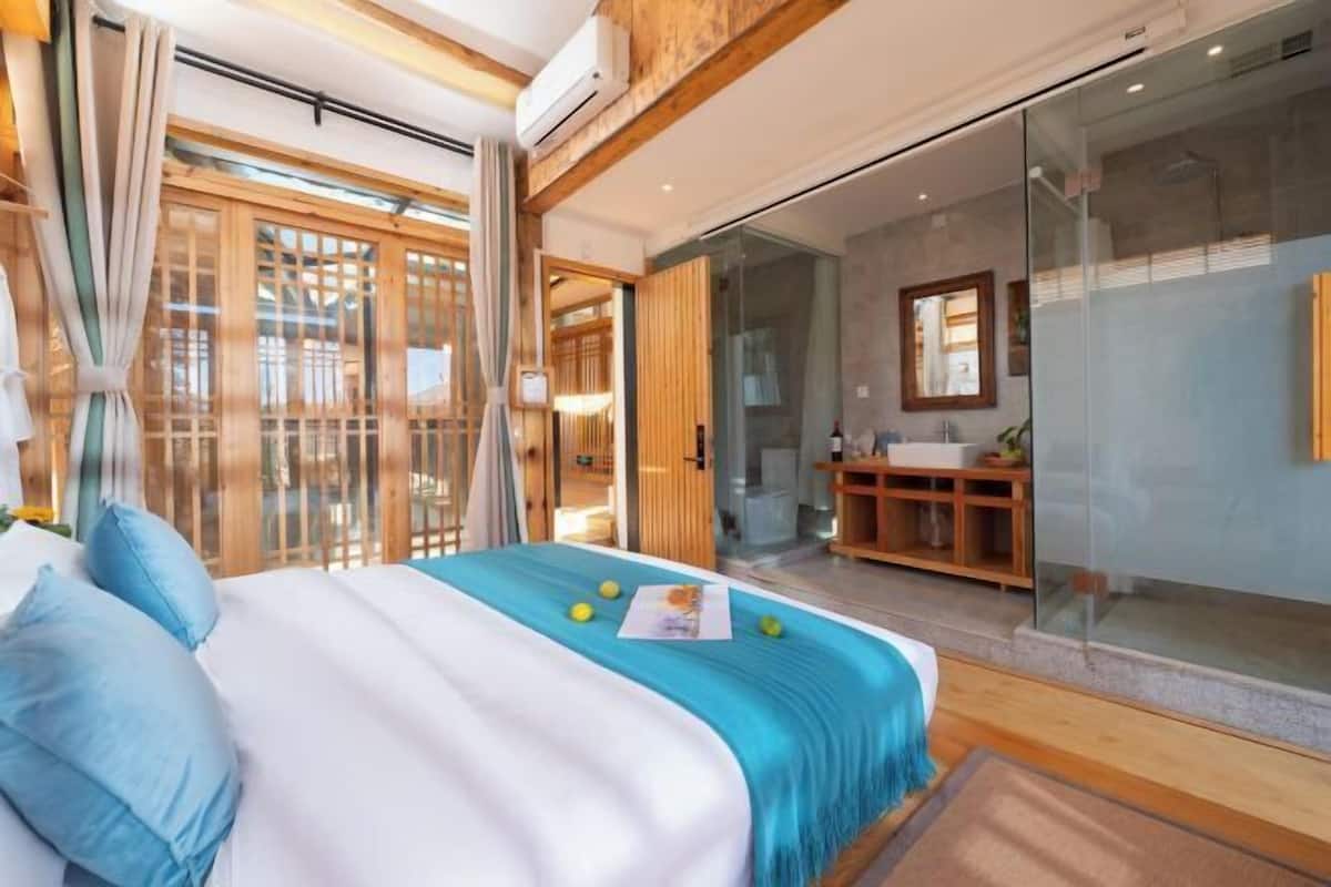 Una habitación de hotel moderna con una cama grande, cabina de ducha de vidrio y un armario de madera.