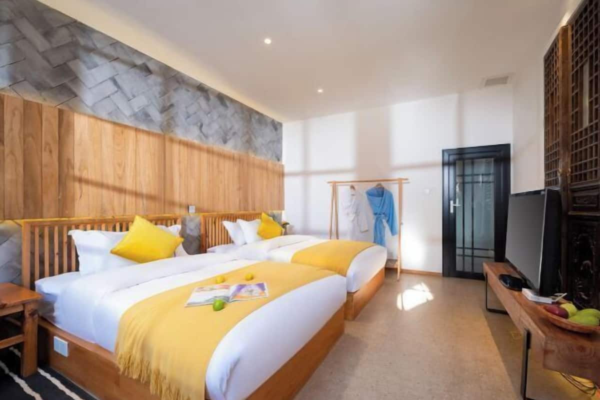 Habitación de hotel con dos camas, cabecero de madera, un banco, un televisor y un armario.