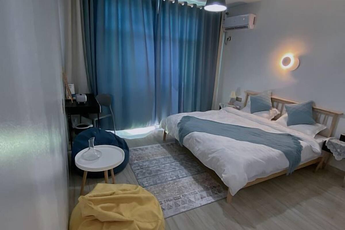 Una habitación de hotel con una cama, una mesita redonda pequeña, una silla, un escritorio y una ventana con cortinas.