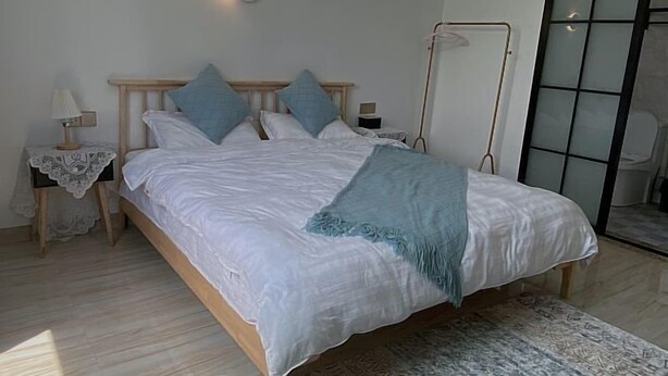 Ein Schlafzimmer mit einem hölzernen Bett, weißer Bettwäsche, einer blauen Tagesdecke und einem Nachttisch mit einer Lampe.
