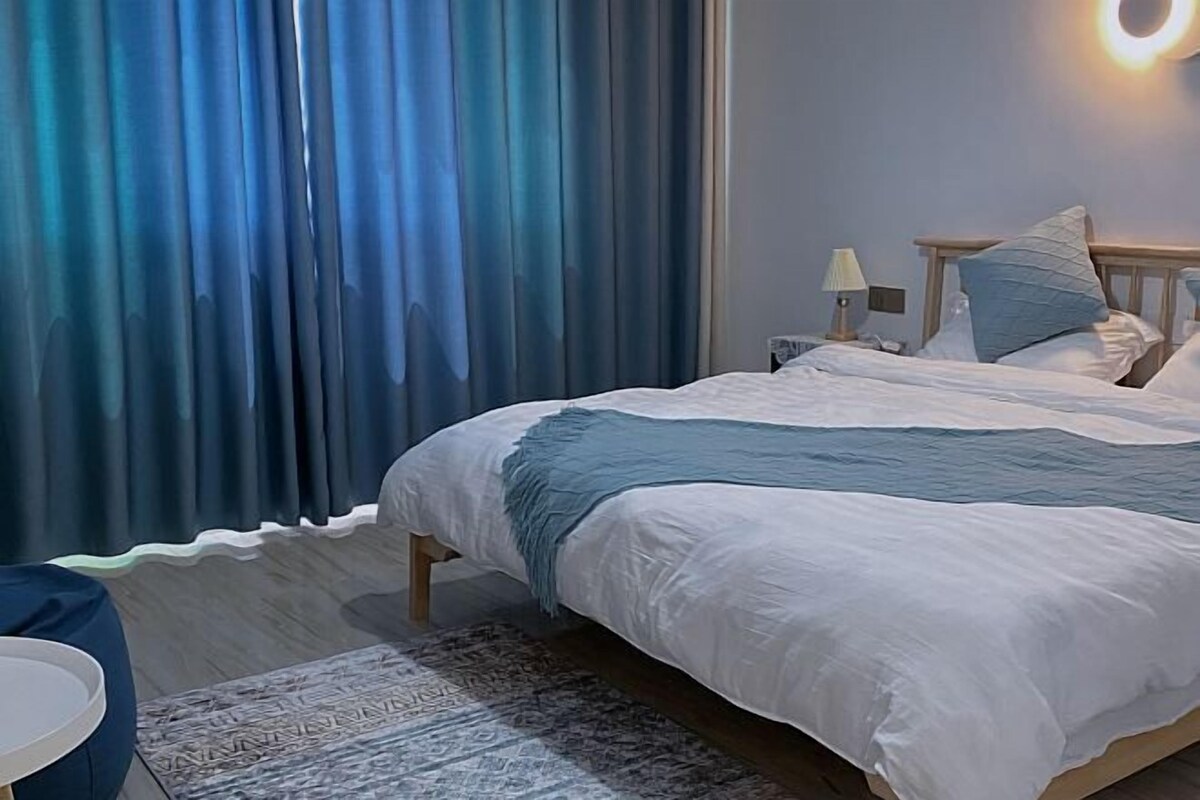 A bedroom with a bed, a nightstand, a lamp, and a ring light on the wall.
