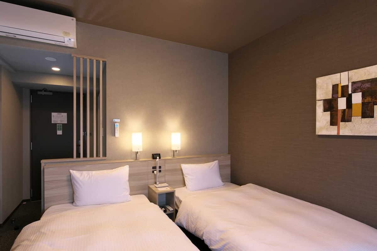 Habitación de hotel con dos camas, una obra de arte en la pared y un aire acondicionado instalado en el techo.
