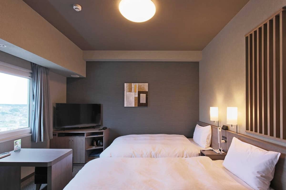 Habitación de hotel con dos camas, televisión, escritorio y ventana.