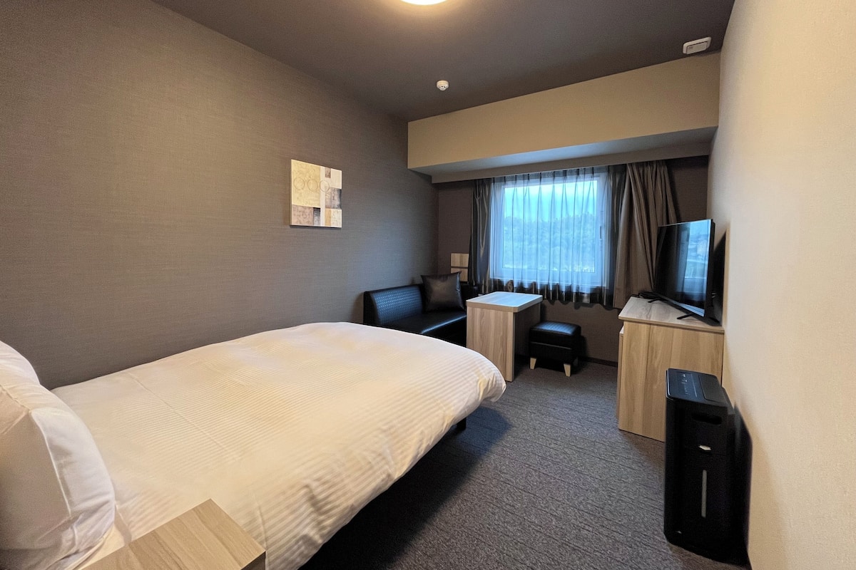 Una habitación de hotel con cama, escritorio, silla, televisión y una pequeña mesa.