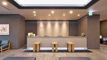 A reception area with a modern design, featuring a reception desk, three wooden stools, a seating area with two sofas, and a tiled wall with the name 'ROUTE NISSAN'.