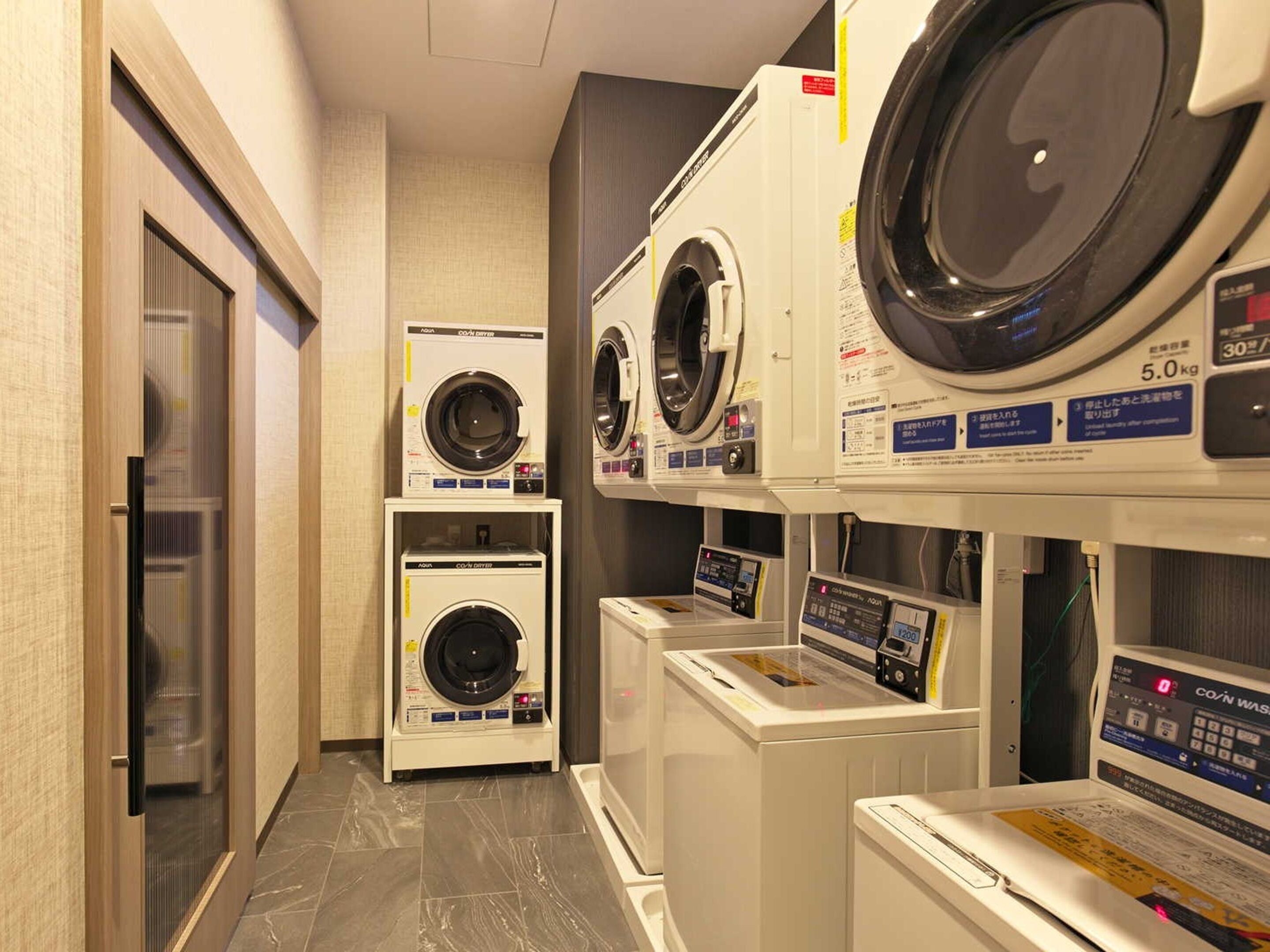 Une buanderie équipée de plusieurs machines à laver et de plusieurs séchoirs, dont une machine à laver à chargement frontal et un sèche-linge à chargement par le haut.