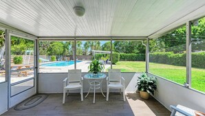 A covered patio with a glass table and chairs, a pool in the background, and a potted plant. - PARADISE RETREAT A 3/2 PET FRIENDLY POOL HOUSE (Bradenton)