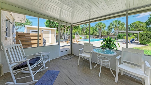 A covered patio with white wicker furniture, a glass door leading outside, and a view of a swimming pool and outdoor area. - PARADISE RETREAT A 3/2 PET FRIENDLY POOL HOUSE (Bradenton)