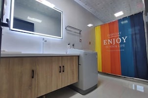 Un baño moderno con tocador de madera, un espejo grande y una pared colorida con texto motivacional.