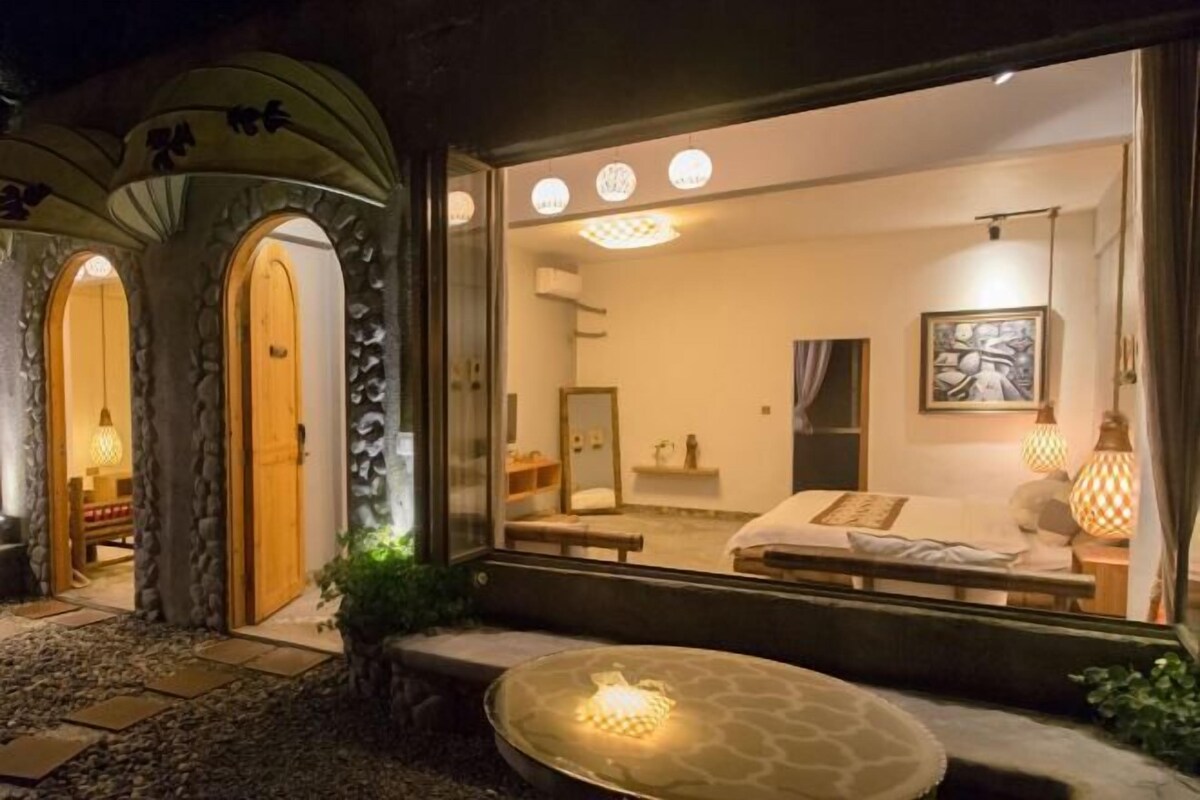 A modern hotel room with a large bed, a bedside table, a mirror, and a window.