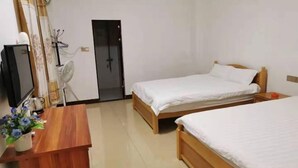 Ein Hotelzimmer mit zwei Einzelbetten, einem Holztisch mit Pflanze, einem Fernseher und einer Tür zu einem Badezimmer.