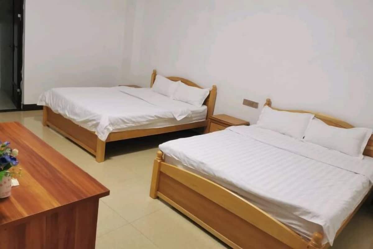 A room with two wooden beds, a wooden desk, and a small table with a vase of flowers.