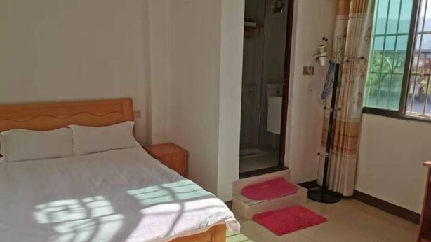 Ein Schlafzimmer mit einem Holzbett, einem kleinen Nachttisch, einer Duschkabine und einem Fenster mit Vorhängen.