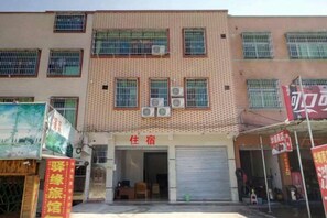 A multi-story building with a ground-level entrance, air conditioning units, and a closed shutter door.