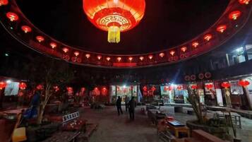 An outdoor seating area with tables and benches, a large red lantern, and a curved ceiling structure.