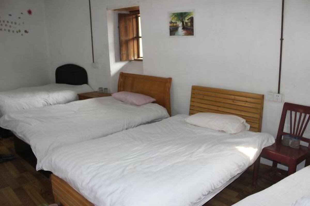 A bedroom with two beds, a wooden headboard, a chair, and a small window.